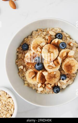 Bowl of porridge topped with banana, blueberries, almonds and cinnamon, a bowl full of oats Stock Photo