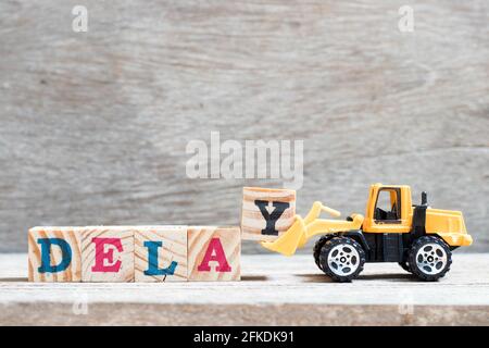 Toy bulldozer hold letter block y to complete word delay on wood background Stock Photo