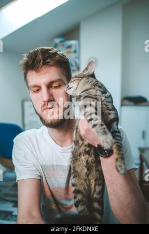 Vertical shot of a bearded Caucasian man holding his clingy cat Stock Photo