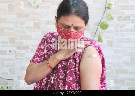 Indian woman looking at bandage applied after getting vaccination during new strain of covid-19, Mature Woman wearing mask received a coronavirus vacc Stock Photo