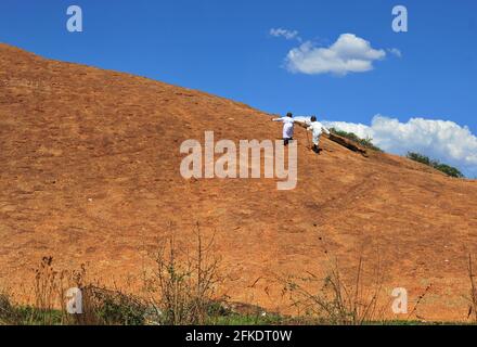 African worshippers going up a rocky hill to pray on clear day with blue sky in Limpopo, South Africa Stock Photo