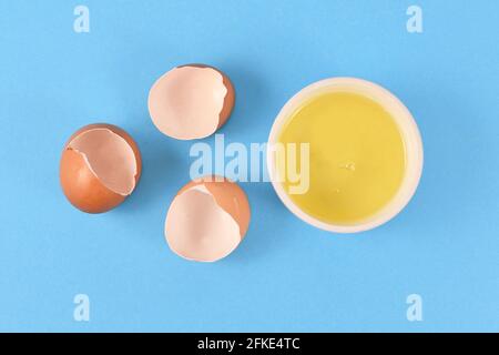 Egg white in bowl next to broken eggshells on yellow background Stock Photo
