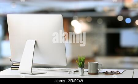 Modern workspace with computer, coffee cup, document and house plant on white desk in office interior. Stock Photo