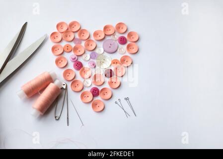 Buttons are lined in the shape of a heart. Two spools of thread. Pins and needle and scissors on a white background. Copy space. Stock Photo