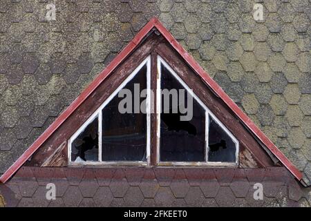 The dormer with damaged glass in the windows on a older roof. Stock Photo