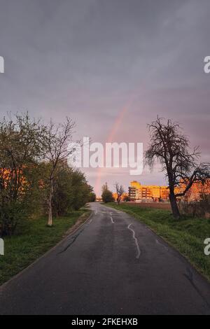 Road to city against rainbow above buildings during spring rain. Prague, Czech Republic Stock Photo