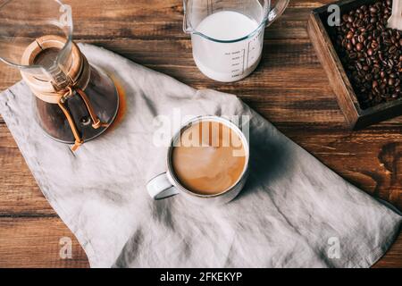 Cup of coffee with milk, milk jug, manual coffee maker and coffee beans on a wooden table Stock Photo