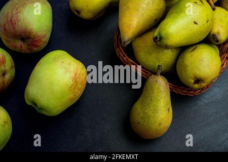 Closeup shot of fresh green pears and apples  on a weaved basket isolated on a dark background Stock Photo