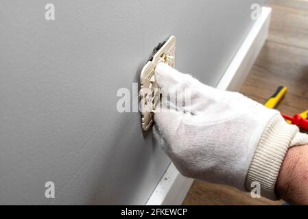 An electrician inserts a double grounded electrical socket into an electrical box in the room wall. Stock Photo