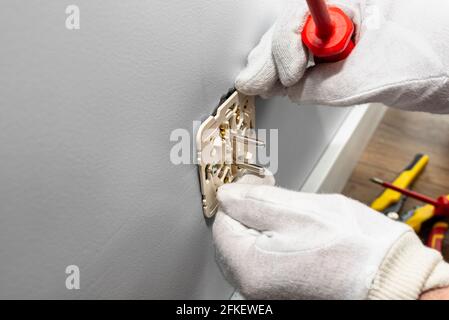 An electrician inserts a double grounded electrical socket into an electrical box in the room wall. Stock Photo