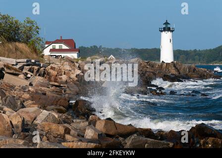 Large waves break over rocky shore by Portsmouth Harbor lighthouse, and nearby keepers quarters, which is now a US Coast Guard station in seacoast New Stock Photo