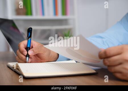 Asian Businessman Writing a business plan After looking at the annual profit and loss summary report.  The concept of Business success Needs to be ana Stock Photo