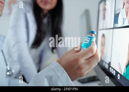Hand of doctor showing vial with new vaccine against coronavirus to his colleagues at online conference Stock Photo