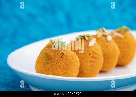 Low Angle Side View Of Indian Subcontinental Special Mithai Motichur Laddu Also Called Motichoor Ladoo Decorated In White Plate On Bright Turquoise Ba Stock Photo