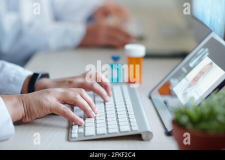 Hands of chief physician working on computer when having online meeting with colleague from another hospital or laboratory Stock Photo