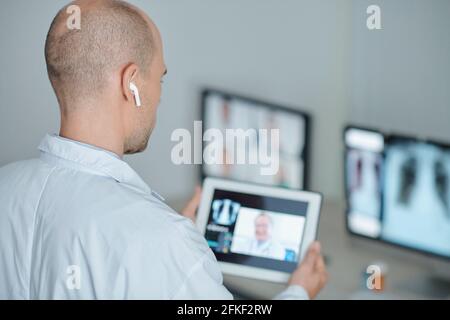 Physician wearing earbuds when making video call to his colleague from another clinic Stock Photo