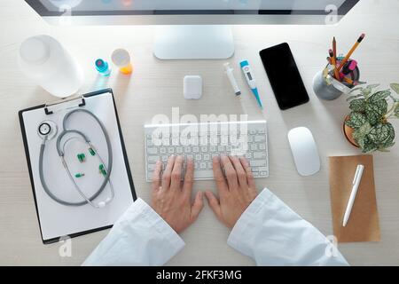 Hands of doctor working on computer at his office desk, view from above Stock Photo