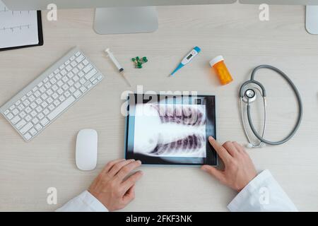 Hands of physician examining chest x-ray on tablet computer, medicine, thermometer and stethoscope are in front of him Stock Photo