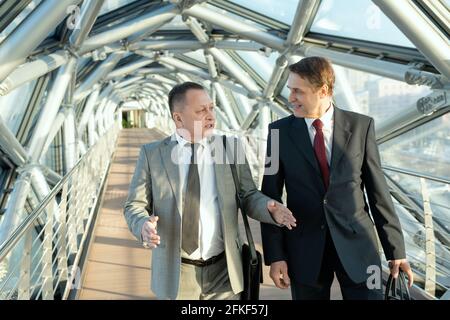 Two confident businessmen in suits walking along modern building Stock Photo