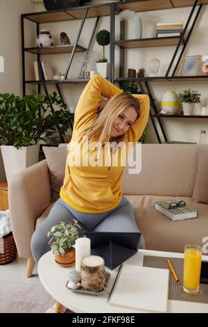 Smiling young woman stretching her back after fishing studying at home Stock Photo