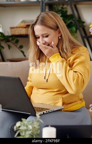 Young woman laughing when watching funny memes and videos on laptop screen Stock Photo
