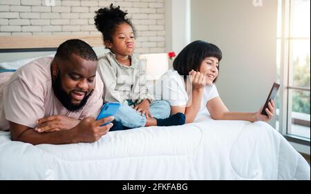 African American girls are not satisfied and sad, sitting in the middle between father and mother. Parents Are using the smartphone and abandoned chil Stock Photo