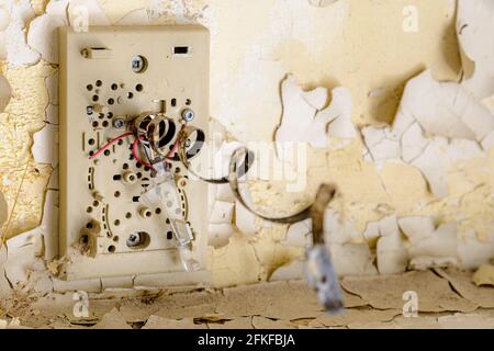 A damaged bi-metallic thermostat on the wall in an abandoned school building. The metallic coil spring is stretched out. Shallow depth of field. Stock Photo
