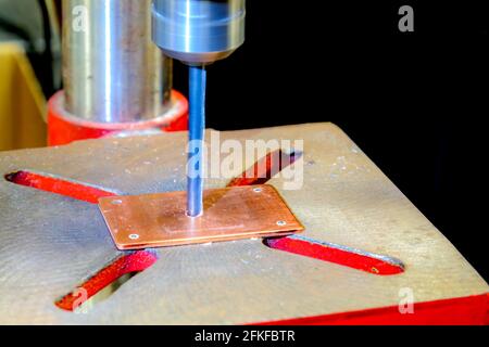 A drill press drilling into a small copper plate. The drill is blurred because it is spinning. Shallow depth of field. Stock Photo