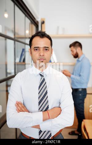 Portrait of serious confident Indian businessman crossing arms and looking at camera when standing in office Stock Photo