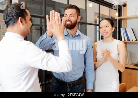 Smiling young businesswoman callping to colleagues giving each other high five after successful meeting Stock Photo