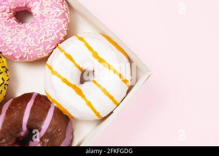 Closeup round colored donuts with sprinkles and topping. Glazed doughnut box. Pastel pink background. Donuts with different flavors Stock Photo