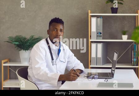 Serious young African American doctor sitting at desk with laptop and looking at camera Stock Photo