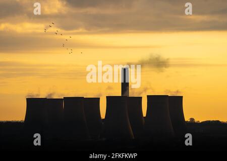 Coal powered electric power station cooling towers chimney silhouette at sunrise dawn with smoke and golden orange sky. Generating electricity supply Stock Photo