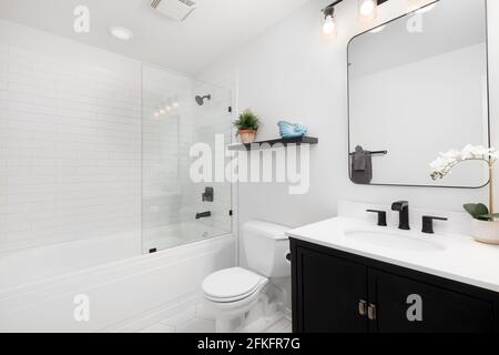 A small modern bathroom with a dark vanity, square mirror,  white subway tiles line the bathtub and shower with black faucets. Stock Photo
