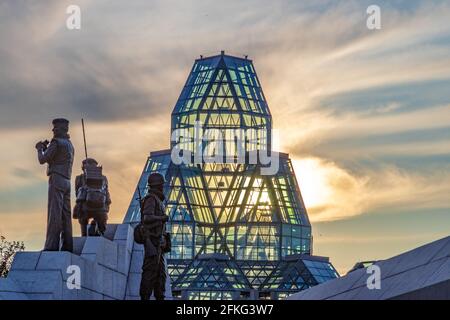 Sunset over a blue glass art gallery with a monument to peacekeepers in the foreground Stock Photo