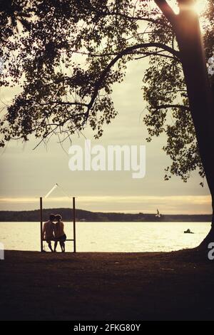 romantic couple sitting on a bench and enjoy the sunset Stock Photo
