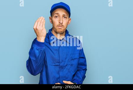 Bald man with beard wearing builder jumpsuit uniform doing italian gesture with hand and fingers confident expression Stock Photo