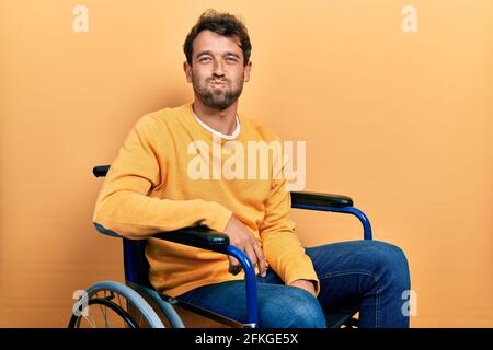 Handsome man with beard sitting on wheelchair puffing cheeks with funny face. mouth inflated with air, crazy expression. Stock Photo