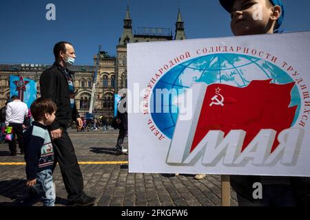 Moscow, Russia. 1st of May, 2021 People walk on Red Square in Moscow during the holiday of Labour Day, also knows as May Day, on the background of a poster. In 2021, in Moscow, the city authorities decided to cancel the May Day traditional demonstration due to the difficult epidemiological situation with the novel coronavirus COVID-19 disease in the region. The inscription on the banner reads 'The 1st May. The International Workers' Solidarity Day' Stock Photo