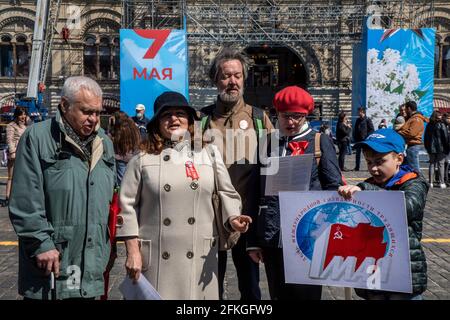 Moscow, Russia. 1st of May, 2021 People sing patriotic songs on Red Square in Moscow during the holiday of Labour Day, also knows as May Day, on the background of decorated Red Square. In 2021, in Moscow, the city authorities decided to cancel the May Day traditional demonstration and celebration due to the difficult epidemiological situation with the Covid-19 disease in the region. The inscription on the banner reads 'The 1st May. The International Workers' Solidarity Day' Stock Photo