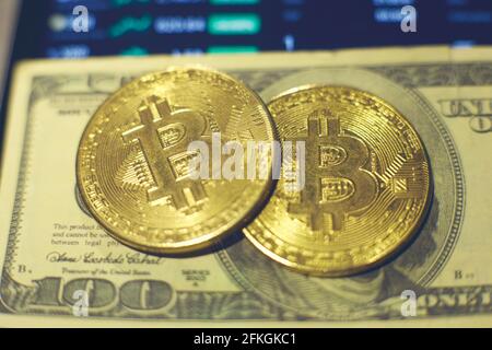 Two gold bitcoin coins lie on a hundred dollar bill. Changes in cryptocurrency rates are shown on the tablet screen Stock Photo