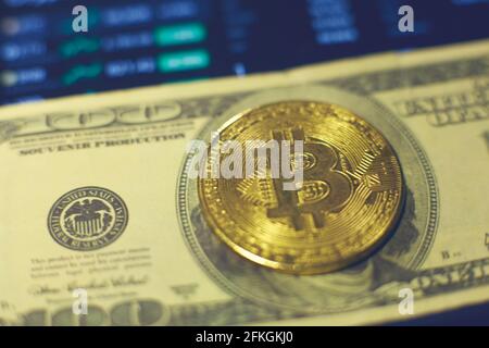 A gold bitcoin coin lies on a hundred dollar bill. Changes in cryptocurrency rates are shown on the tablet screen Stock Photo