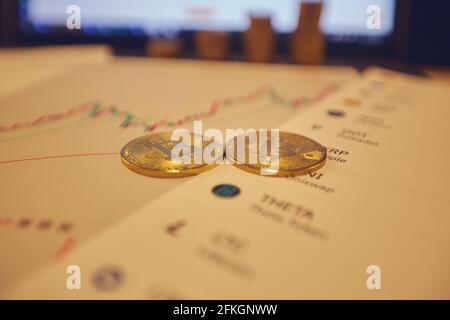 Two gold bitcoins are on the graphs of cryptocurrency rate changes on a laptop. In the background, several rows of coins and a laptop screen. Stock Photo