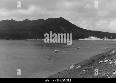 Grayscale shot of small boats sailing on water surrounded by hills Stock Photo