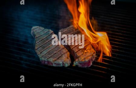 Two pieces of Striploin beef tips on getting grilled on a barbeque grill. Stock Photo