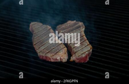 Two pieces of Striploin beef tips on getting grilled on a barbeque grill. Stock Photo