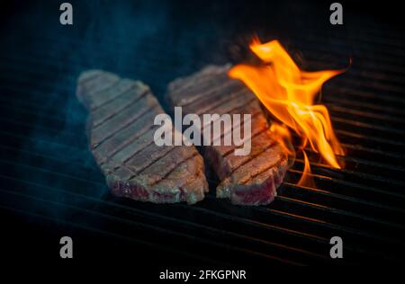 Two pieces of Striploin beef tips on getting grilled on a barbeque grill. Stock Photo