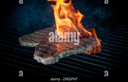 Two pieces of Striploin beef tips on getting grilled on a barbeque grill. Stock Photo