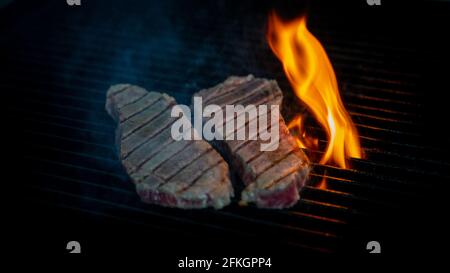 Two pieces of Striploin beef tips on getting grilled on a barbeque grill. Stock Photo