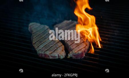 Two pieces of Striploin beef tips on getting grilled on a barbeque grill. Stock Photo